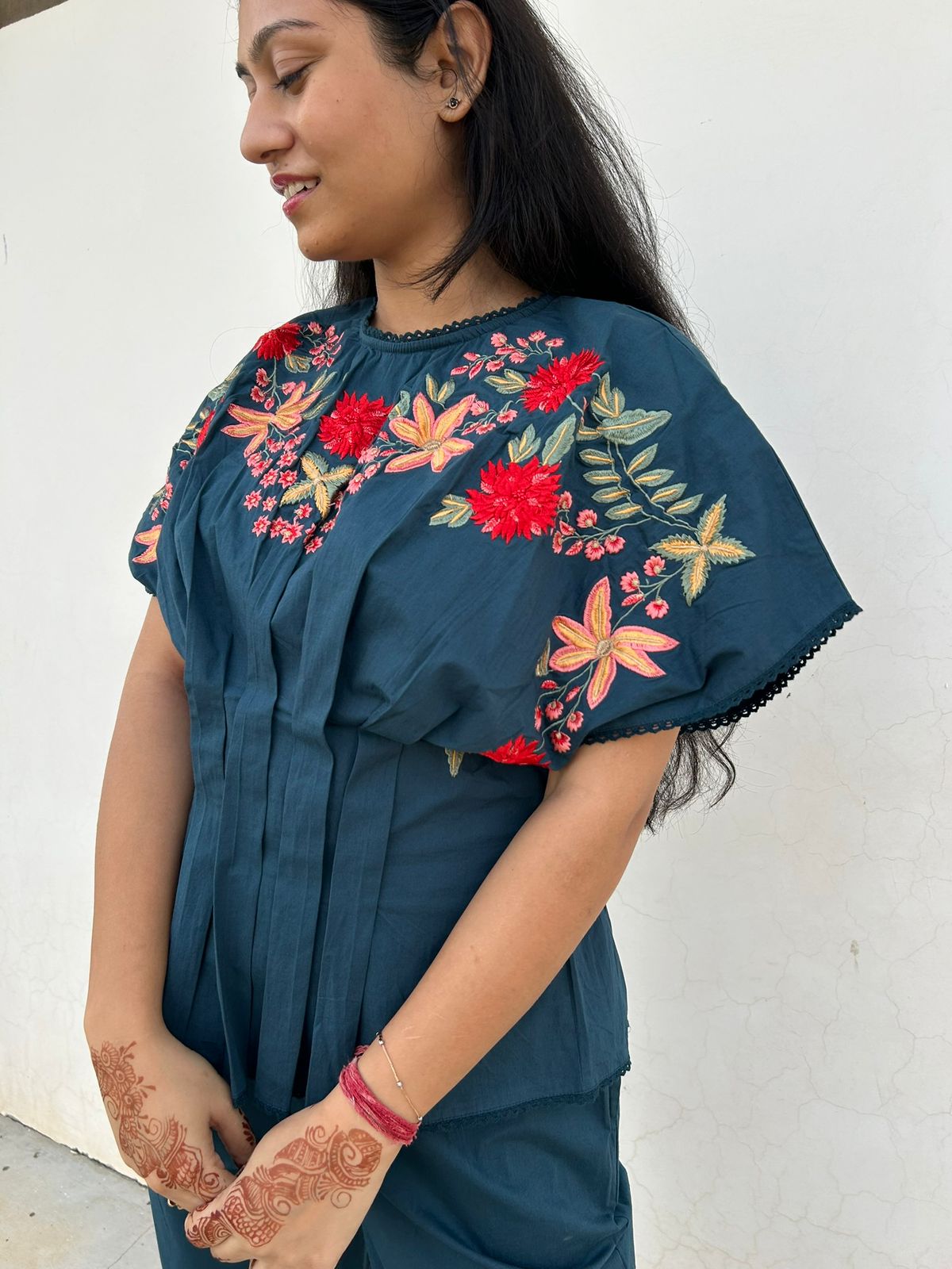 Woman wearing a teal top with floral embroidery against a white background